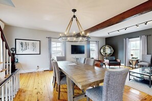 A dining area with a wooden table, chairs, a chandelier, and a large mirror. - Charming, historic cottage with modern upgrades - stroll to dining & attractions (Boothbay Harbor)