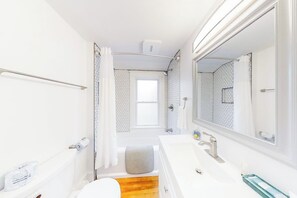 A compact bathroom with a shower, toilet, and sink, featuring a wooden floor and a large mirror. - Mill Pond Cottage w/ Kayaks & Boat Launch Access, pet friendly (East Boothbay)