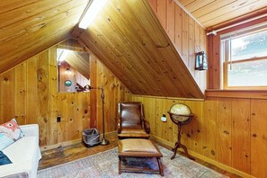 Ein gemütliches Dachzimmer mit Holzwänden, Holzbalkendecke, einem Sessel, einem kleinen Tisch mit Globus und einem Fenster.