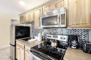 A kitchen with stainless steel appliances, wooden cabinets, a tiled backsplash, and a coffee maker. - Water-view condo at Sheepscot Harbour Resort with deck, full kitchen, and WiFi (Edgecomb)