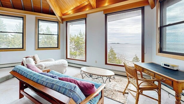 Quarto com cama, escrivaninha e janelas amplas com vista para o exterior.
