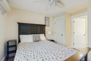 A bedroom with a bed, a nightstand, a ceiling fan, a door, and a wall-mounted air conditioner.