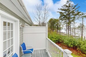 A covered porch with a white railing, a blue chair, and a window with blinds.