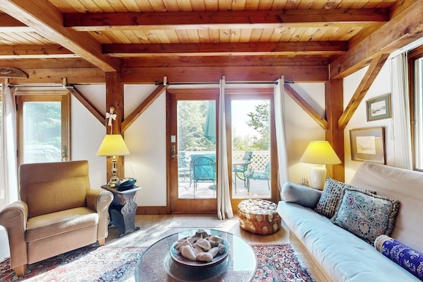 A cozy room with a wooden ceiling, a sofa, a chair, a small table, and a window with curtains.