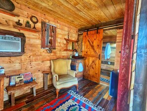 A wooden cabin interior with a chair, a small table, a rug, and a door with a mirror.
