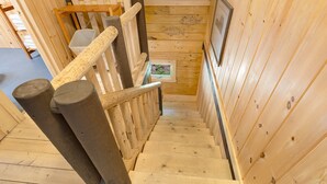 A wooden staircase with a handrail, a small window with a view, and a framed picture on the wall.