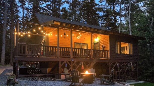 A wooden cabin with a balcony, outdoor seating, and a fire pit.