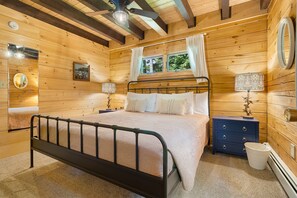 Un dormitorio de cabaña de madera con cama, dos mesitas de noche, un espejo y una ventana.