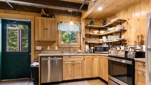 A compact kitchen with wooden cabinets, stainless steel appliances, and a window with a view of greenery.