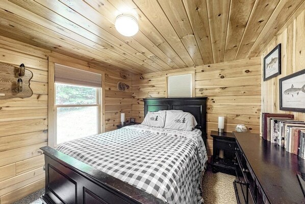 Ein Schlafzimmer einer Holzhütte mit Bett, Nachttisch und Wandleuchte.