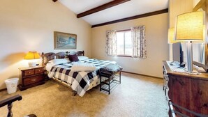 Quarto com cama, mesa de cabeceira, penteadeira, abajur e janela com cortinas.