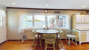 A room with a round table, four chairs, a window with a view of a dock, and a white cabinet.