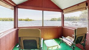 A covered seating area with two chairs and a small table, overlooking a body of water and a dock.