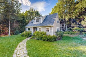 A two-story house with a stone pathway leading to the front door, surrounded by lush greenery and trees. - Open and spacious riverfront retreat, dog-friendly (St. George)
