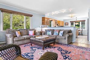 A living room with a sofa, ottoman, and wicker chairs, a kitchen with wooden cabinets, and large windows. - Waterfront Oasis - Charming home with stunning bay views, sunroom, gazebo, deck (Trenton)