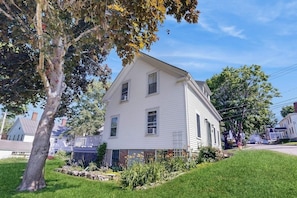 Ein weißes, zweistöckiges Haus mit Vorgarten, Baum und angrenzenden Häusern.