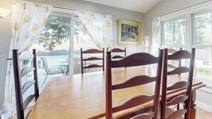 Un comedor con mesa y sillas de madera, un cuadro en la pared y vistas por la ventana.
