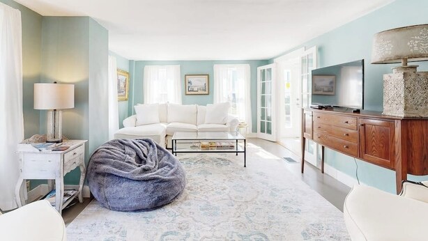 Una habitación con un sofá blanco, un sillón informal, una mesa de centro, un televisor y un mueble de madera.