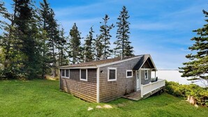 A small cabin with a porch, surrounded by a grassy yard and tall trees. - Dog-friendly oceanfront cottage with views (St. George)