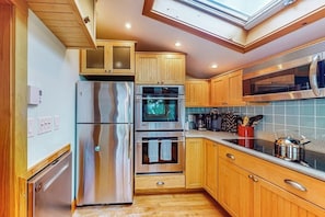 A modern kitchen with stainless steel appliances, wooden cabinets, and a skylight.