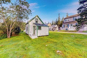 A small, single-story house with a green roof and white siding, surrounded by a well-maintained lawn and trees.
