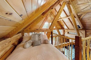 Ein Holzinnenraum mit hoher Decke, einem Bett mit gemustertem Überwurf und einem Holgeländer.