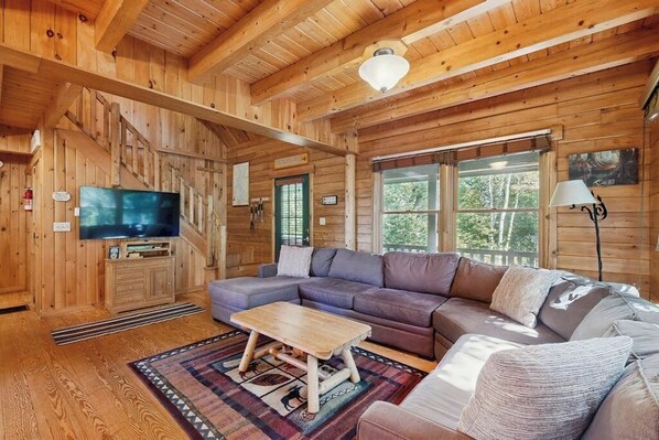 Ein Holzblockhaus-Interieur mit einem großen Fernseher, einer Couch, einem Couchtisch und einem Kamin.