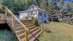 A cabin with a wooden staircase leading to a deck, surrounded by dense forest. - Sea View- Dog-friendly bay view home - water views (Boothbay Harbor)