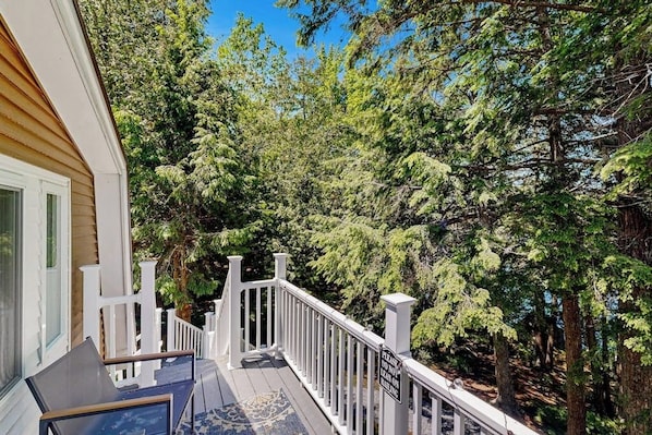 A wooden deck with white railings, surrounded by dense green trees. - Charming Lakefront Apartment with Deck, Patio and BBQ Grill (Orland)