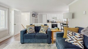 Ein Wohnzimmer mit einem blauen Sofa, einem Couchtisch und einer Küche im Hintergrund.