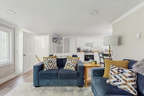 A living room with a blue sofa, a coffee table, and a kitchen in the background. - Charming Lakefront Apartment with Deck, Patio and BBQ Grill (Orland)