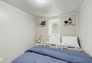 A bedroom with a bed, a window, a nightstand, and a shelf with a plant and a bottle. - Charming Lakefront Apartment with Deck, Patio and BBQ Grill (Orland)