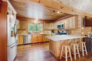 A wooden cabin interior with a kitchen featuring wooden cabinets, a central island with stools, a stainless steel refrigerator, and a microwave. - 10-acre waterfront hideaway with kayak, private dock on Prong Pond & firepit (Greenville)