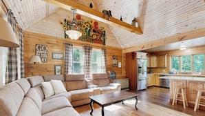 Un intérieur de chalet chaleureux avec un canapé d’angle, un plancher en bois, un coin cuisine et un espace repas.