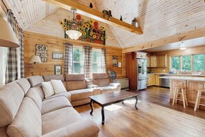 Ein gemütliches Blockhaus-Interieur mit einer Eckcouch, Holzböden, einer Küchenzeile und einem Essbereich.