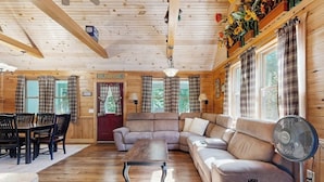 L’intérieur d’une cabane en rondins comprend un coin repas, un canapé, un ventilateur et un sapin de Noël.