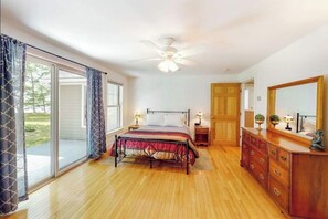 A bedroom with a bed, a dresser, a nightstand, a ceiling fan, and a sliding glass door leading to a patio. - Secluded lakefront home with patio & firepit, fast WiFi, wood stove & W/D (Ellsworth)