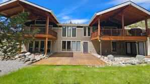 Een twee verdiepingen tellend huis met een houten terras, grote ramen en een balkon.