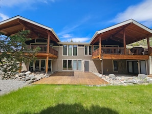 Ein zweigeschossiges Haus mit einer Holzterrasse, großen Fenstern und einem Balkon.