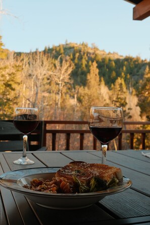 Une table à manger avec une assiette de nourriture et deux verres à vin, le tout placé devant un paysage de colline boisée.