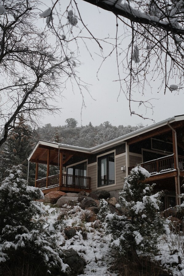 A cabin with a wooden deck, large windows, and a stone foundation. - Spacious & serene 4-bdrm country house with backyard creek in charming Sheridan (Sheridan)