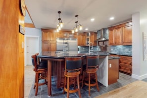 Una cocina moderna con armarios de madera, una isla central con taburetes de bar, electrodomésticos de acero inoxidable y un salpicadero con azulejos azules.