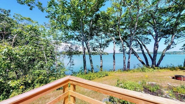 A wooden deck with a view of a lake and trees. - Rising Tide Cottage- Waterfront home on St. George River with private beach & deck - near festivals (Cushing)