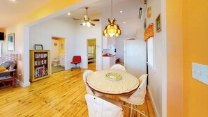 A room with a round dining table, white chairs, a ceiling fan, a bookshelf, and a red chair. - Rising Tide Cottage- Waterfront home on St. George River with private beach & deck - near festivals (Cushing)