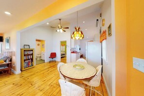 A room with a round dining table, white chairs, a ceiling fan, a bookshelf, and a red chair.