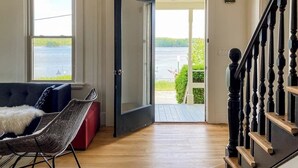 Ein Zimmer mit Blick auf ein Gewässer, eine Tür, die nach draußen führt, eine Treppe und ein Sofa mit einer kuscheligen Decke.