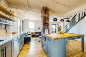 A modern kitchen with a central island, wooden flooring, and a brick accent wall.