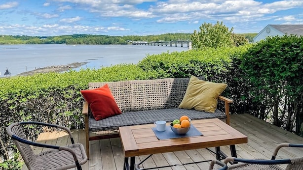Eine Terrasse mit einer Rattan-Couch, einem Tisch mit Obst und Blick auf eine Brücke über dem Wasser.