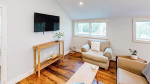 Un salon avec un plancher en bois, un canapé, une table basse, un téléviseur fixé au mur et une fenêtre.