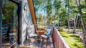Une terrasse en bois avec des meubles d’extérieur, une porte vitrée et une vue sur les arbres.